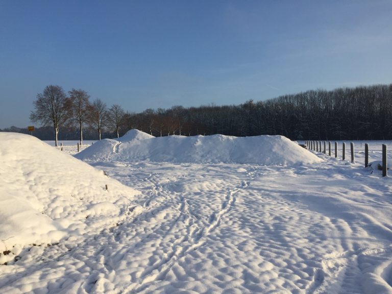 Schneebedeckte Erdhügel und im Hintergrund ein Wald.