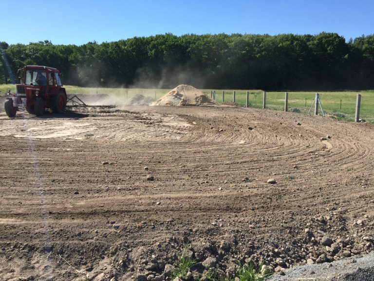 Ein roter Traktor ebnet einen staubtrockenen Acker.